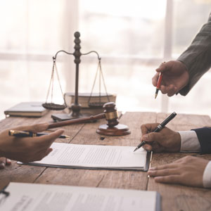 Hands signing legal documents on a table with scales of justice symbolizing Legal Jargon